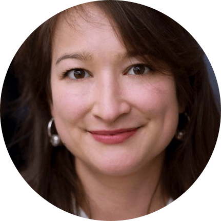 Portrait of a person with long brown hair, wearing hoop earrings, smiling slightly, against a dark background.