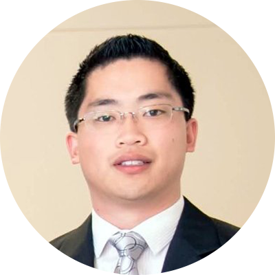 A person with short black hair wearing glasses and a suit, posing for a portrait against a neutral background.