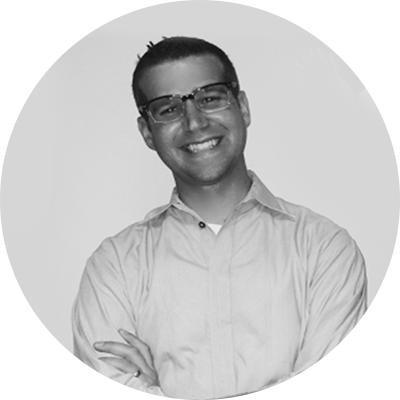 A person wearing glasses and a button-up shirt smiles with arms crossed.